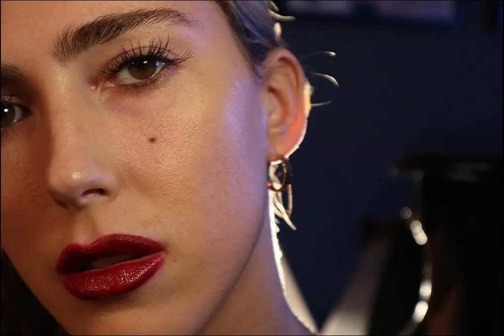 Close-up of a woman's face with bold red lipstick and unique earrings.