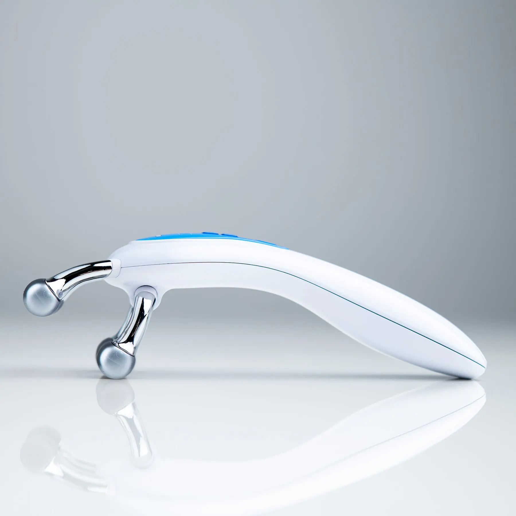 A sleek white handheld massager with dual roller heads on a reflective surface.