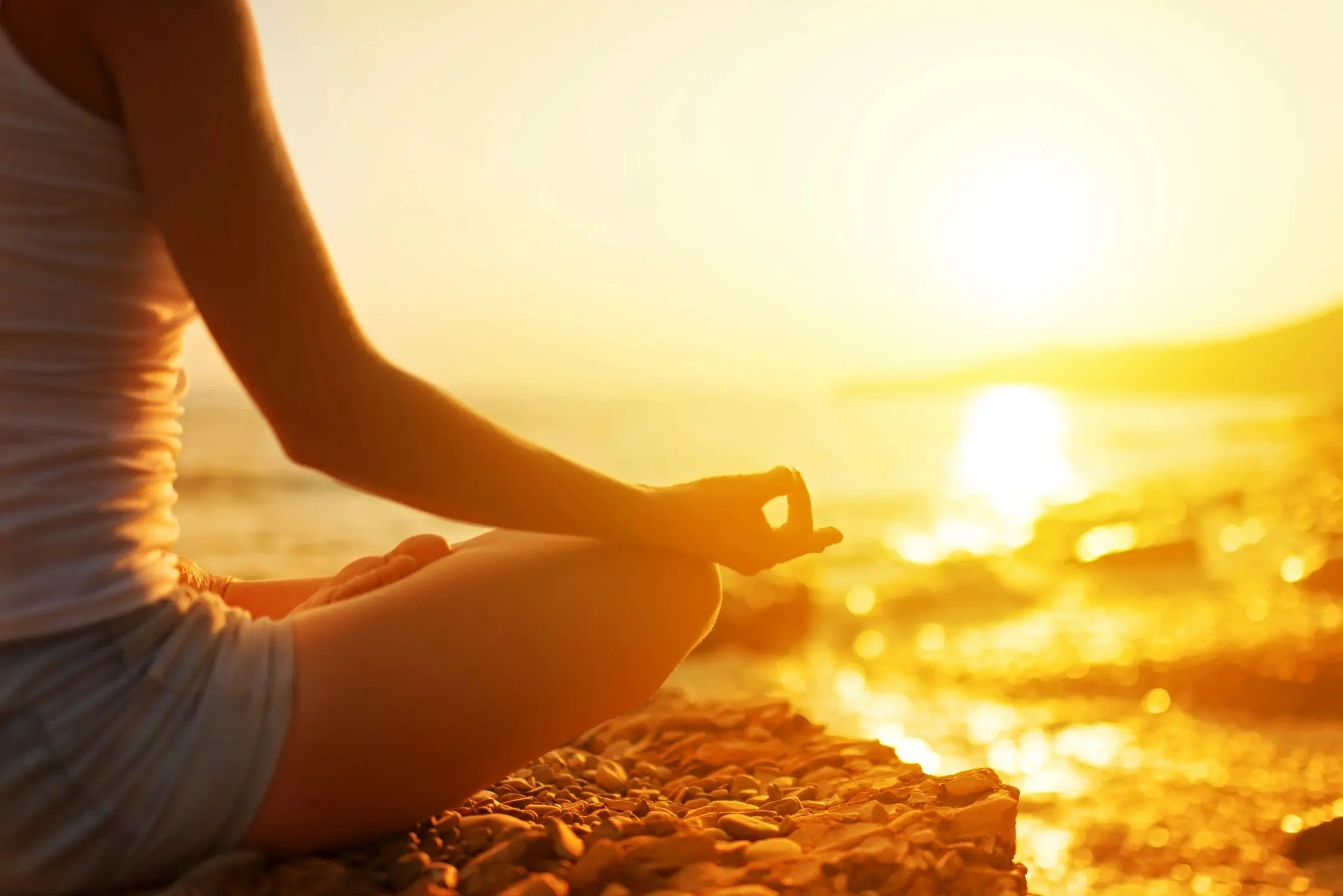 Person meditating by the water at sunset, practicing mindfulness.