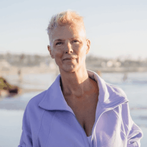 A woman in a light purple jacket standing near a beach on a sunny day.